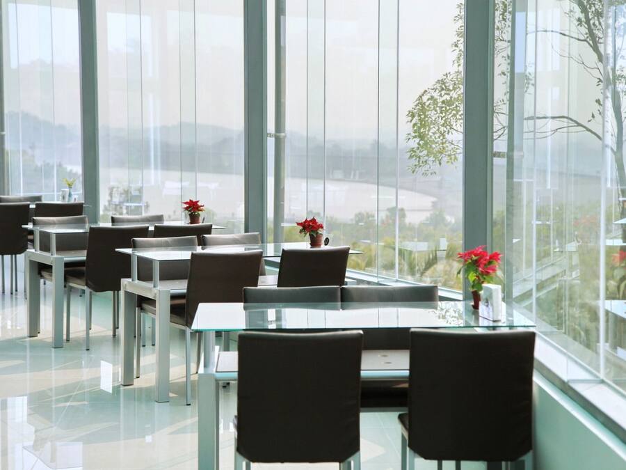 A modern dining area with glass tables and chairs, large windows, and potted plants.