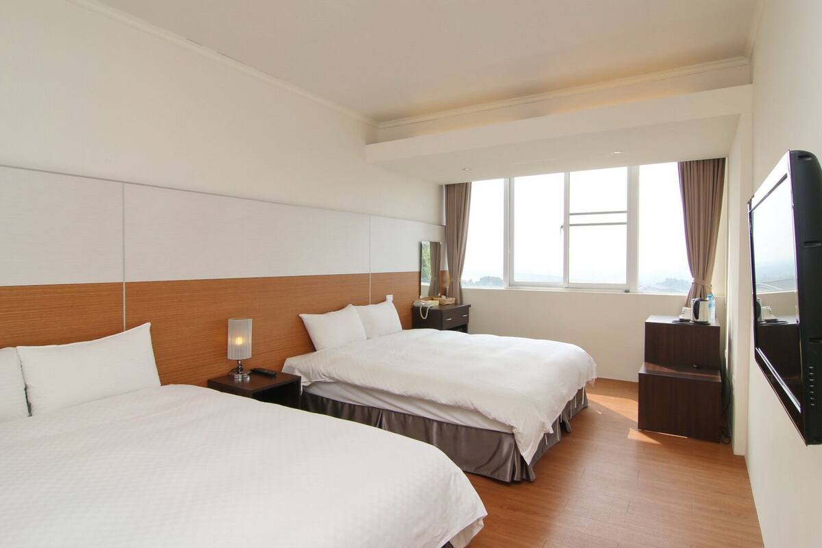Ein Hotelzimmer mit zwei Betten, einem Fernseher, einem Nachttisch und einem Fenster mit Blick.