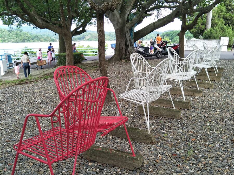 Outdoor seating under trees with a lake view.