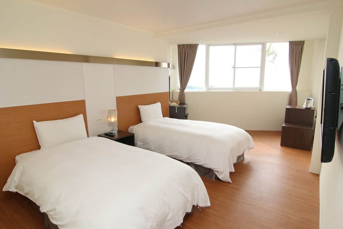 Ein Hotelzimmer mit zwei Betten, Holzboden, Fernseher und einem Fenster mit Vorhängen.