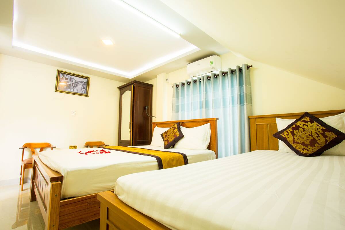 A hotel room with two single beds, a wooden wardrobe, a ceiling light, and a wall-mounted air conditioner.
