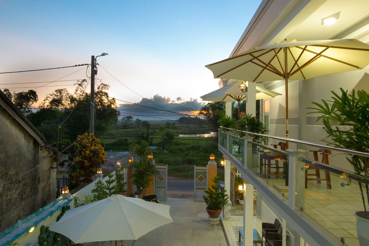 A hotel balcony with outdoor seating, a view of the surrounding landscape, and a gated entrance.