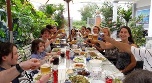 A group of people seated around a table with various dishes and drinks, outdoors with greenery in the background. - Riverside Pottery Village (Da Nang)
