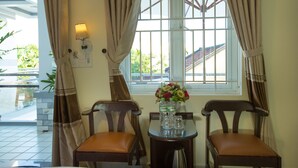 Una habitación con dos sillas de madera, una mesita con un florero y una ventana con cortinas.