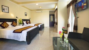 Habitación de hotel con dos camas, un sofá, un televisor y una mesa de centro de vidrio con flores y botellas.