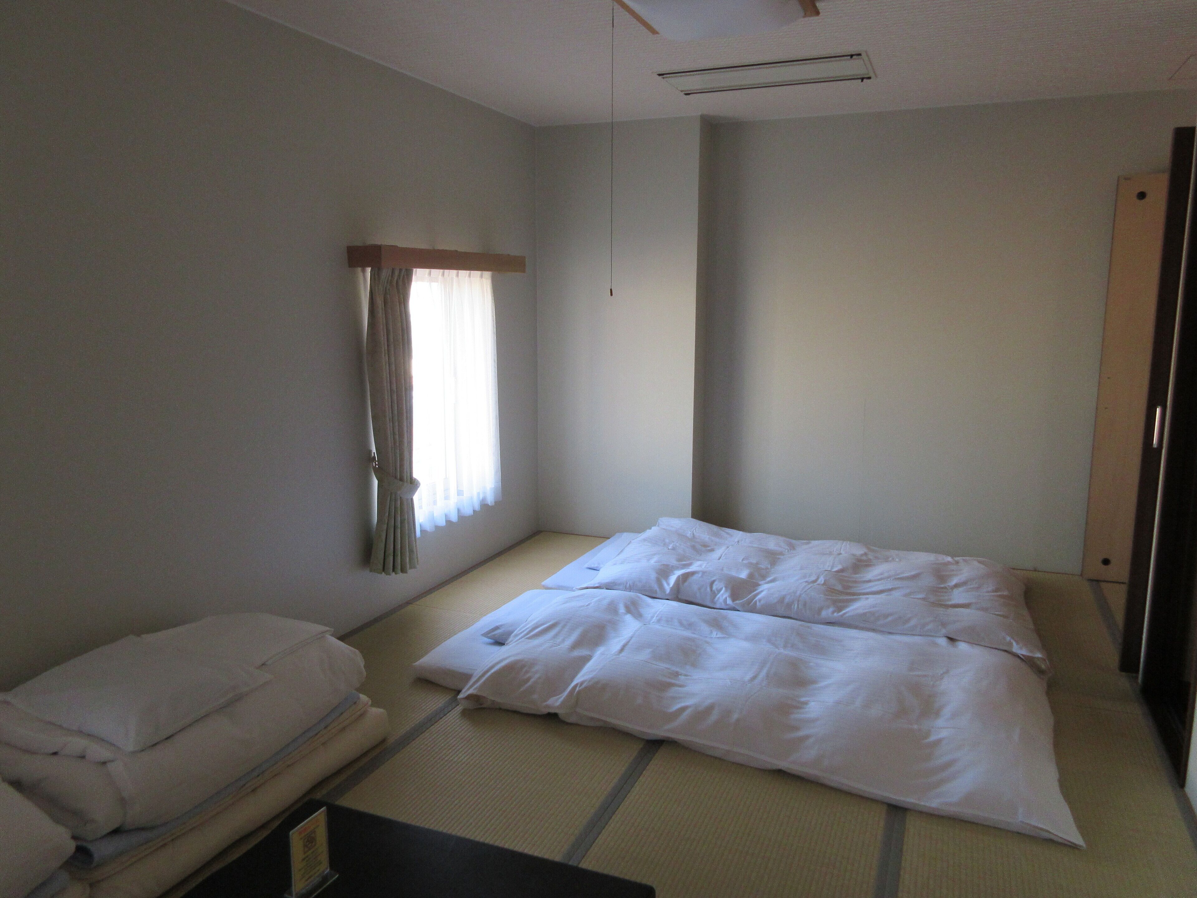 Una habitación de hotel con cama, una silla y un ventanal con cortinas.