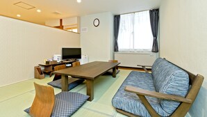 A room with tatami flooring, a wooden table, a sofa, a television, and a clock on the wall. - Hotel New Ohte (Hakodate)
