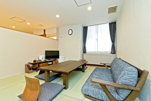 Una habitación con suelo de tatami, una mesa de madera, un sofá, un televisor y un reloj en la pared.