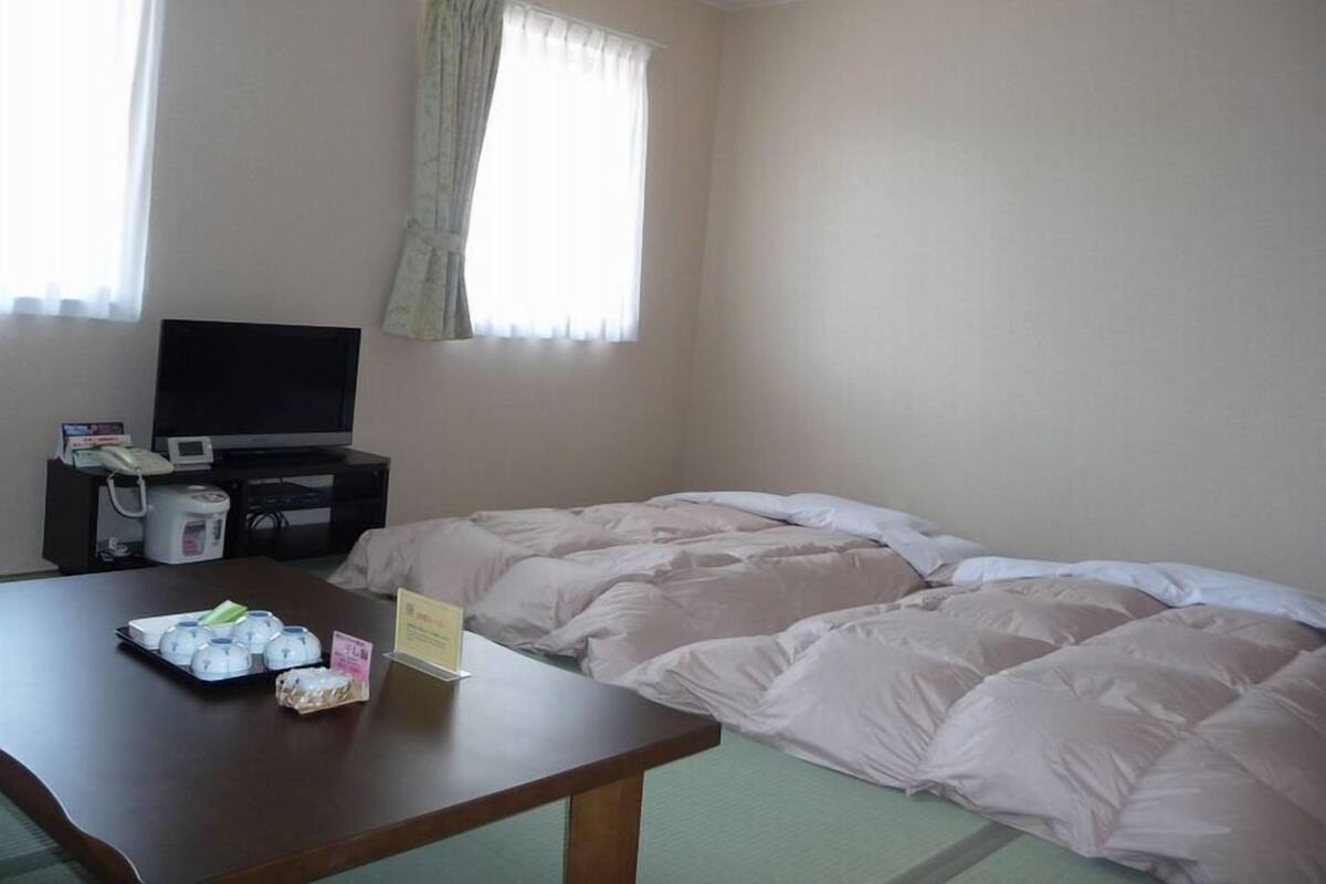 A hotel room with a bed, a TV, a table with food items, and a window with curtains.