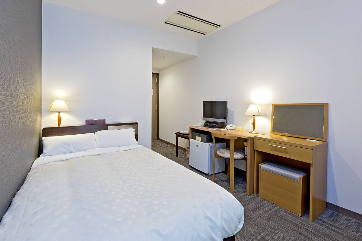 A hotel room with a bed, desk, chair, television, and desk lamp.