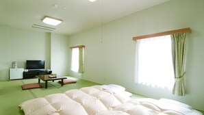 A room with tatami flooring, a bed with multiple pillows, a television, a small refrigerator, and a window with curtains. - Hotel New Ohte (Hakodate)