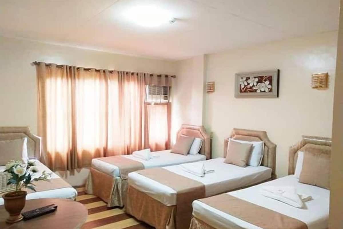 A hotel room with two single beds, a small table with a remote control, a potted plant, and a painting on the wall.