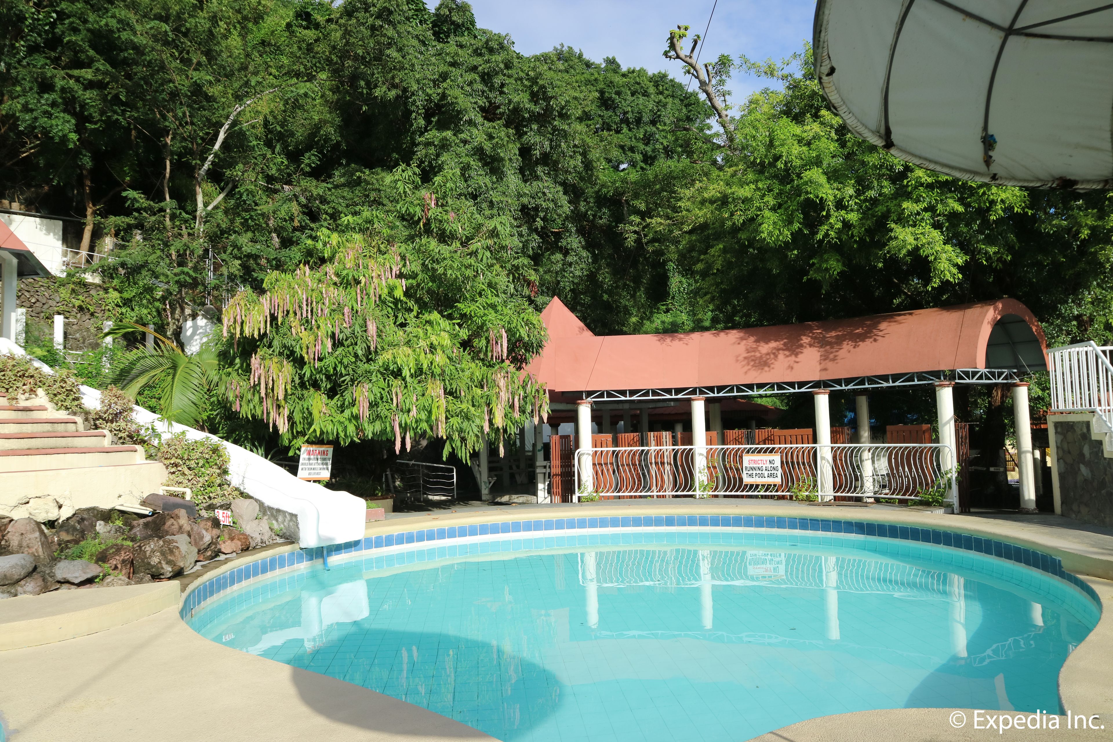 Piscina con un área de descanso cubierta, rodeada de abundante vegetación y una escalera que sube.