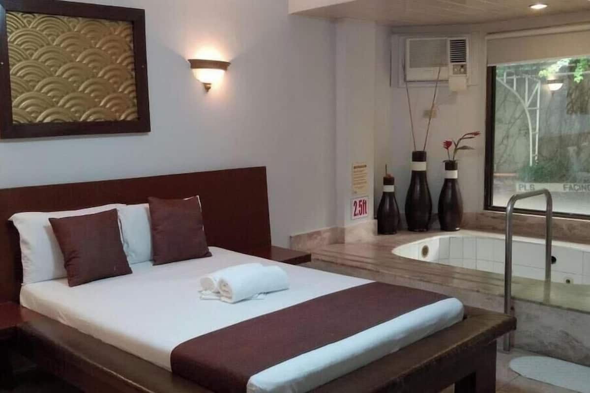 A hotel room with a bed, a bathtub, and a view of trees.