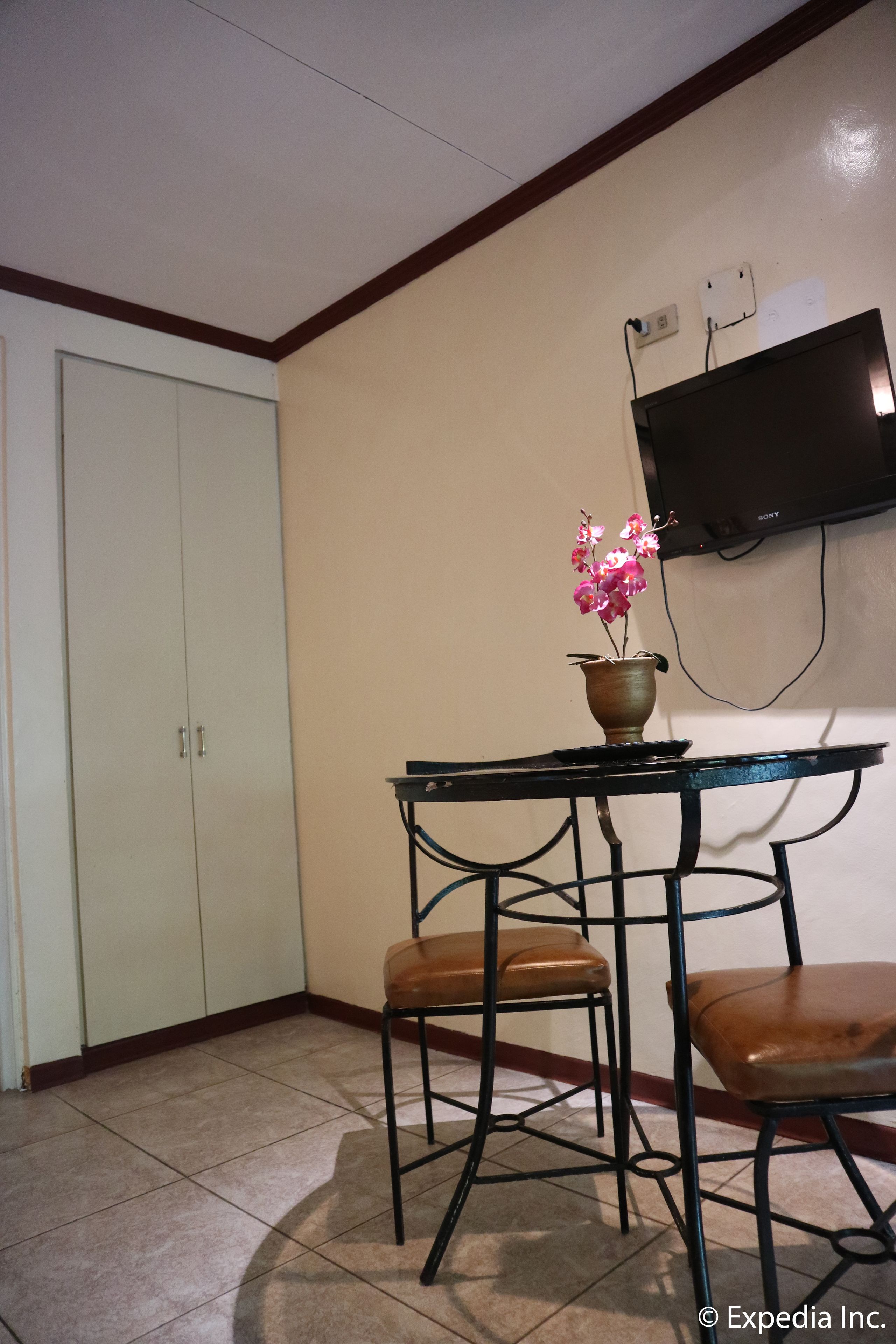 Habitació amb taula de dinar, dues cadires, una orquídia en test, televisió penjada a la paret i un armari.