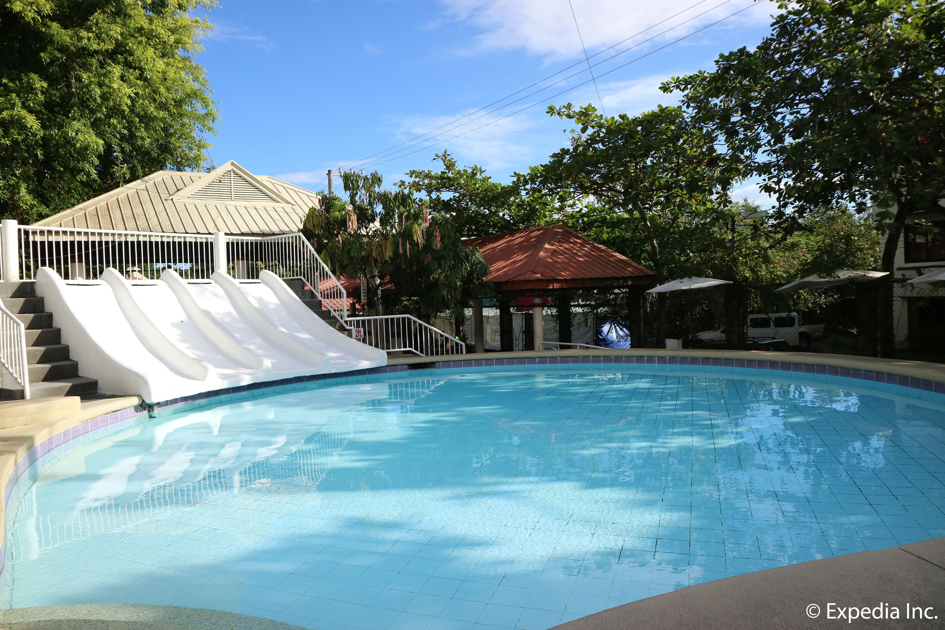 A swimming pool with a slide, a gazebo, and a covered area with umbrellas.