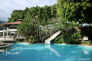 Ein Swimmingpool mit Rutsche, umgeben von üppiger Vegetation und einem Gebäude mit rotem Dach.