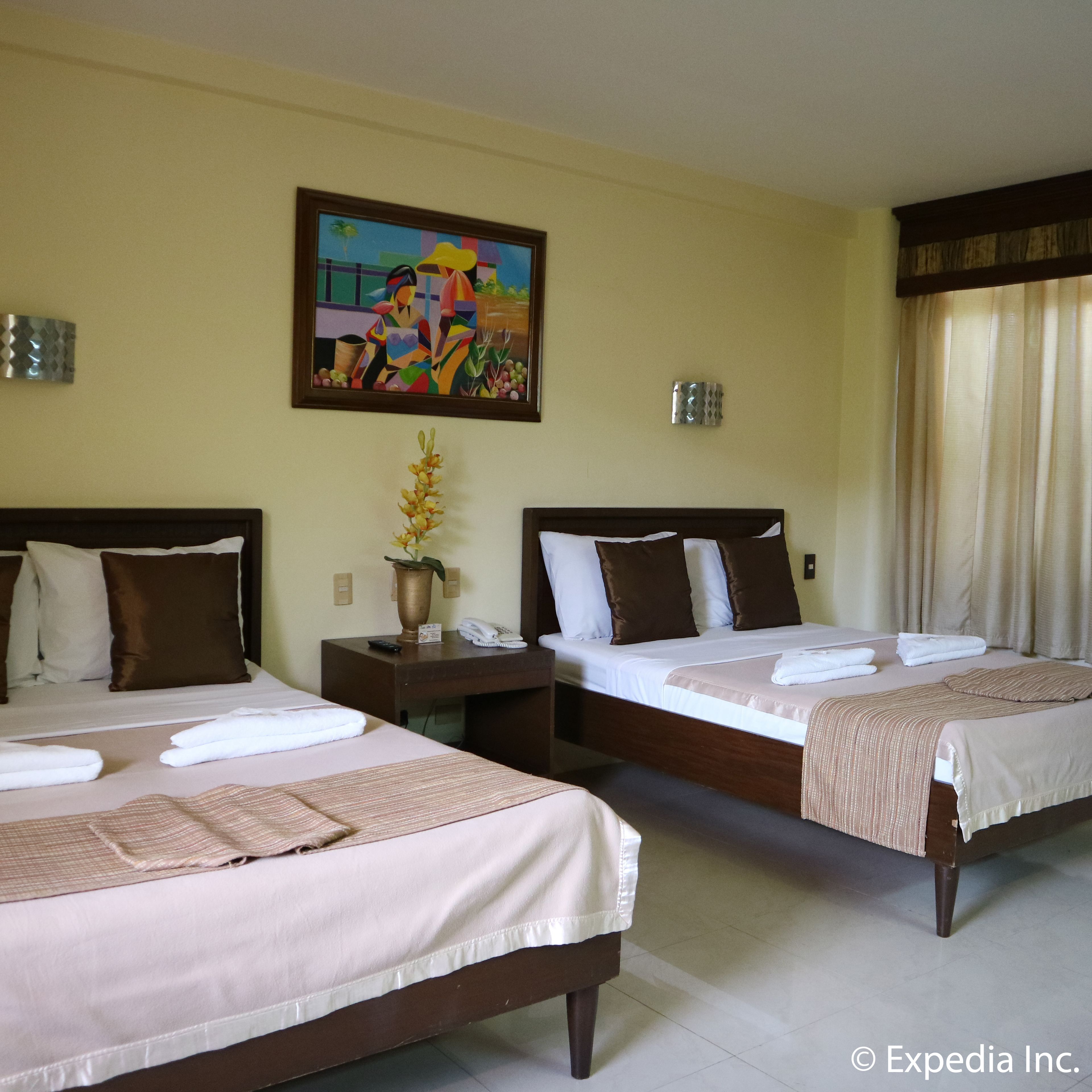 Quarto de hotel com duas camas, um quadro na parede e um vaso com flores.