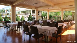 A spacious outdoor dining area with multiple tables and chairs, surrounded by large windows and a view of a building with balconies. - Splash Oasis Resort Hotel (Los Banos)