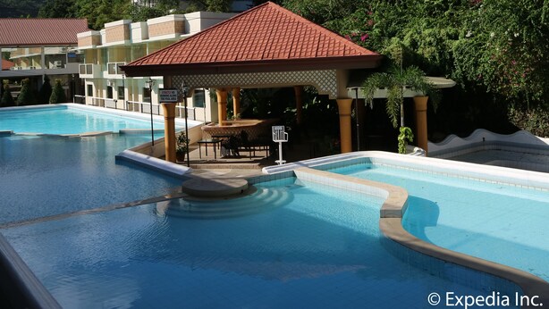 A hotel with multiple swimming pools, a covered seating area, and lush greenery. - Splash Oasis Resort Hotel (Los Banos)