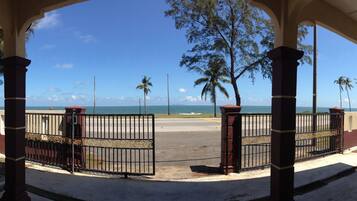 Vista a la playa desde un espacio cubierto con una verja, palmeras y un cartel que dice 'Semarak Beach Inn'.
