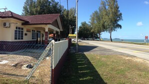 A coastal hotel with a tiled roof, a fenced yard, and a road leading to the beach.