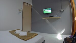 A hotel room with a bed, a television mounted on the wall, a door, and a small shelf.