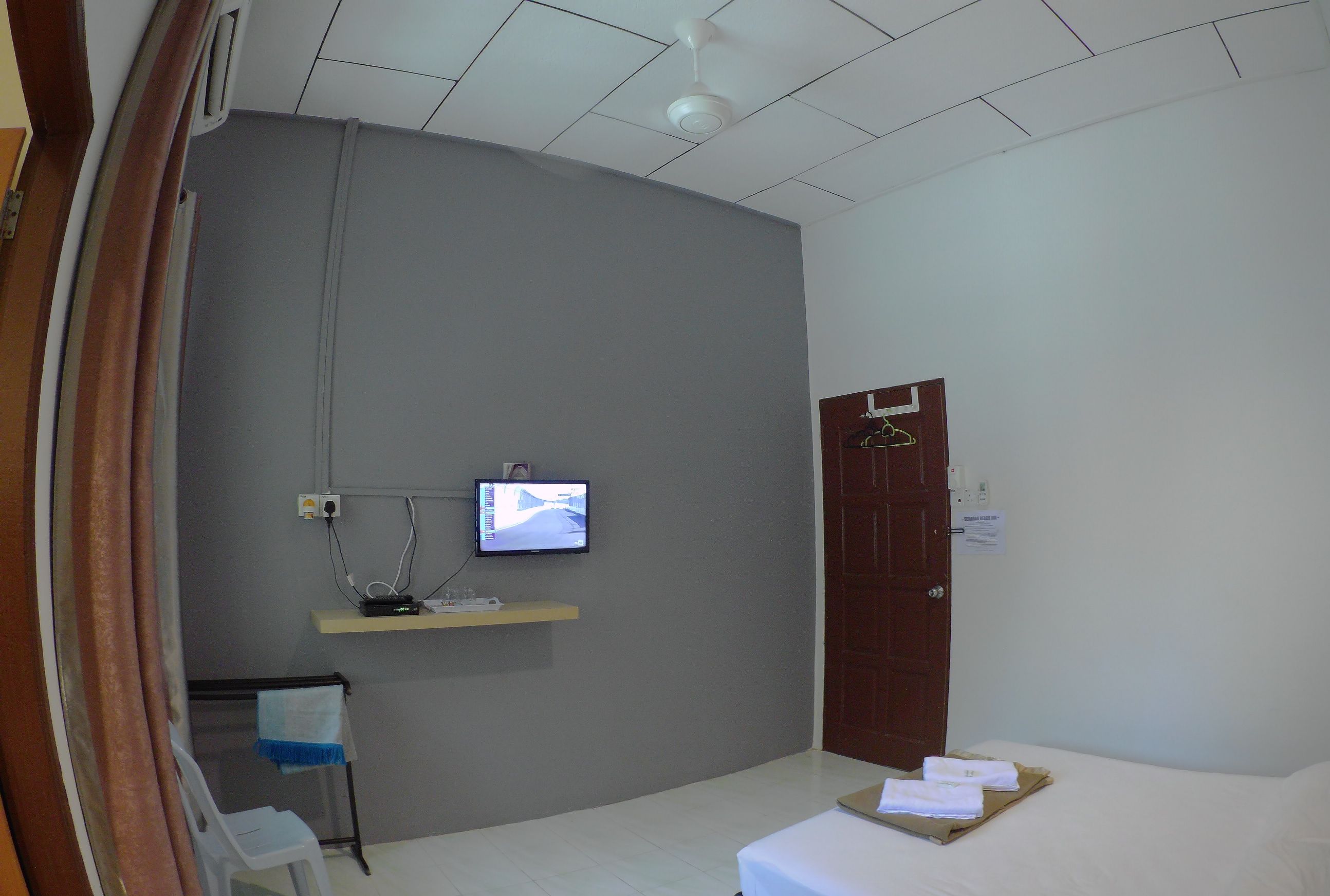 A hotel room with a bed, a television mounted on the wall, a wooden door, and a small shelf with a power outlet.