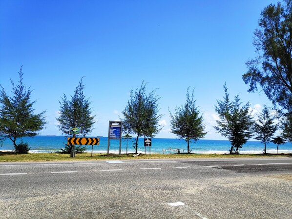 Una carretera con vista a la playa, árboles y un cartel con indicaciones.
