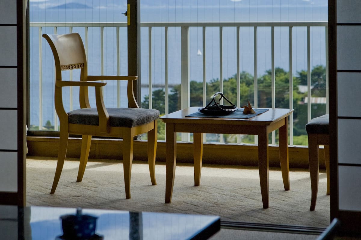 Een balkon met een houten stoel en tafel, uitzicht op bergen en een weerspiegeling op het glas.