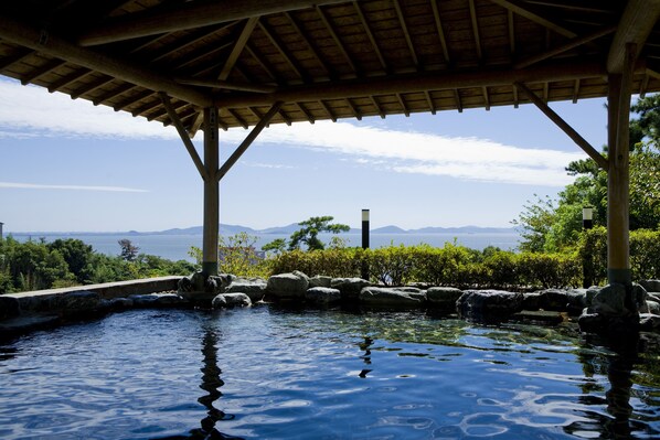 A wooden pergola over a pool with a view of mountains and the sea.