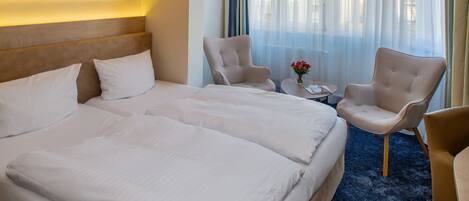 A hotel room with a large bed, two armchairs, a small table with a vase of flowers, and a painting of a lighthouse on the wall.
