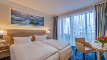 Relax in a serene space with a large bed, a painting of a lighthouse, and a small table with a vase of flowers.