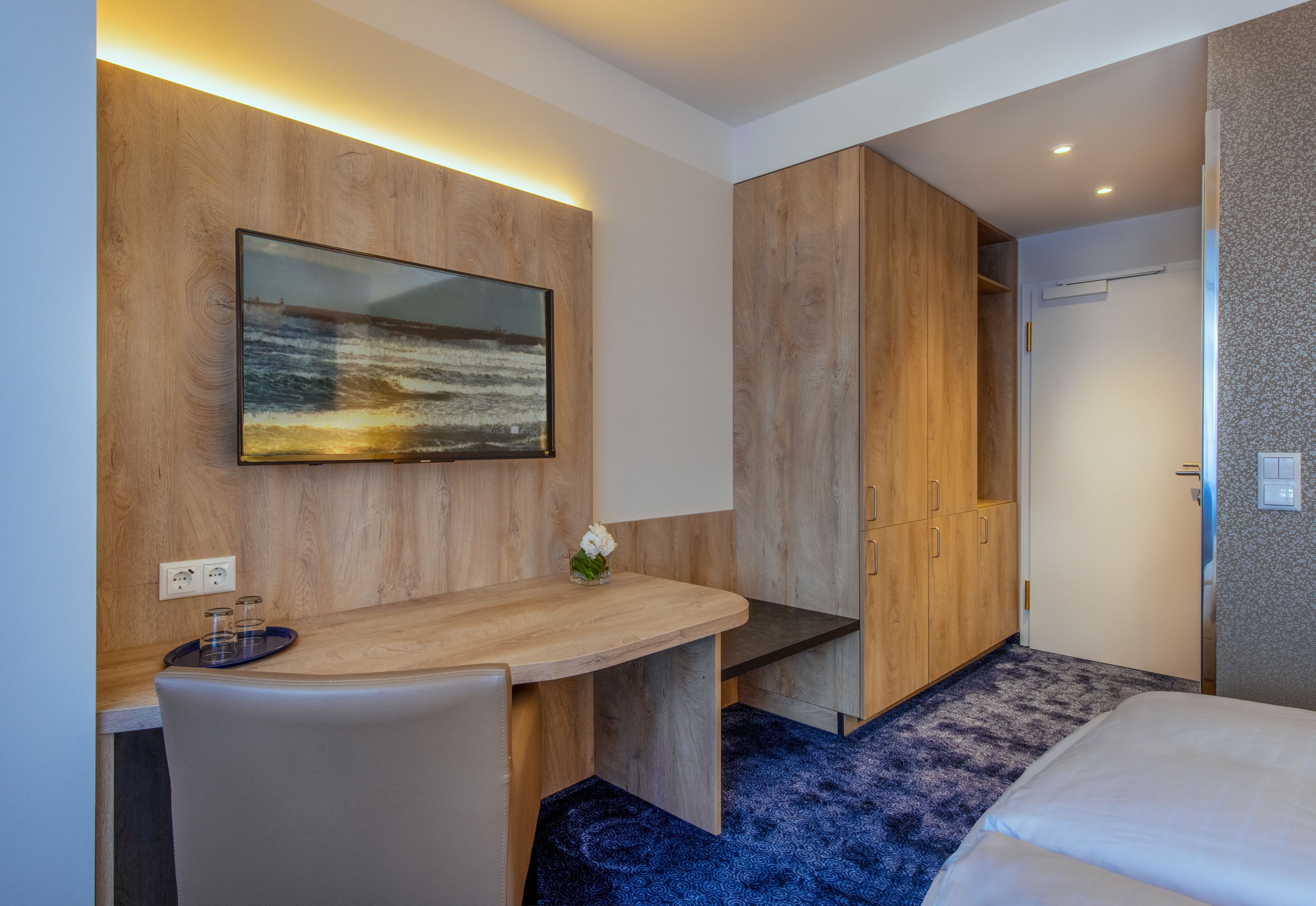 Ett hotellrum med ett skrivbord i trä, en säng och en stor tavla på väggen.