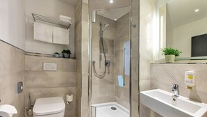 A modern bathroom with a glass-enclosed shower, a toilet, a sink, and a towel rack with folded towels. - Pension StromInn (Rostock)