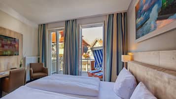 Ein Hotelzimmer mit einem großen Bett, einem Schreibtisch mit Stuhl, einem Fernseher und Blick auf den Außenbalkon.