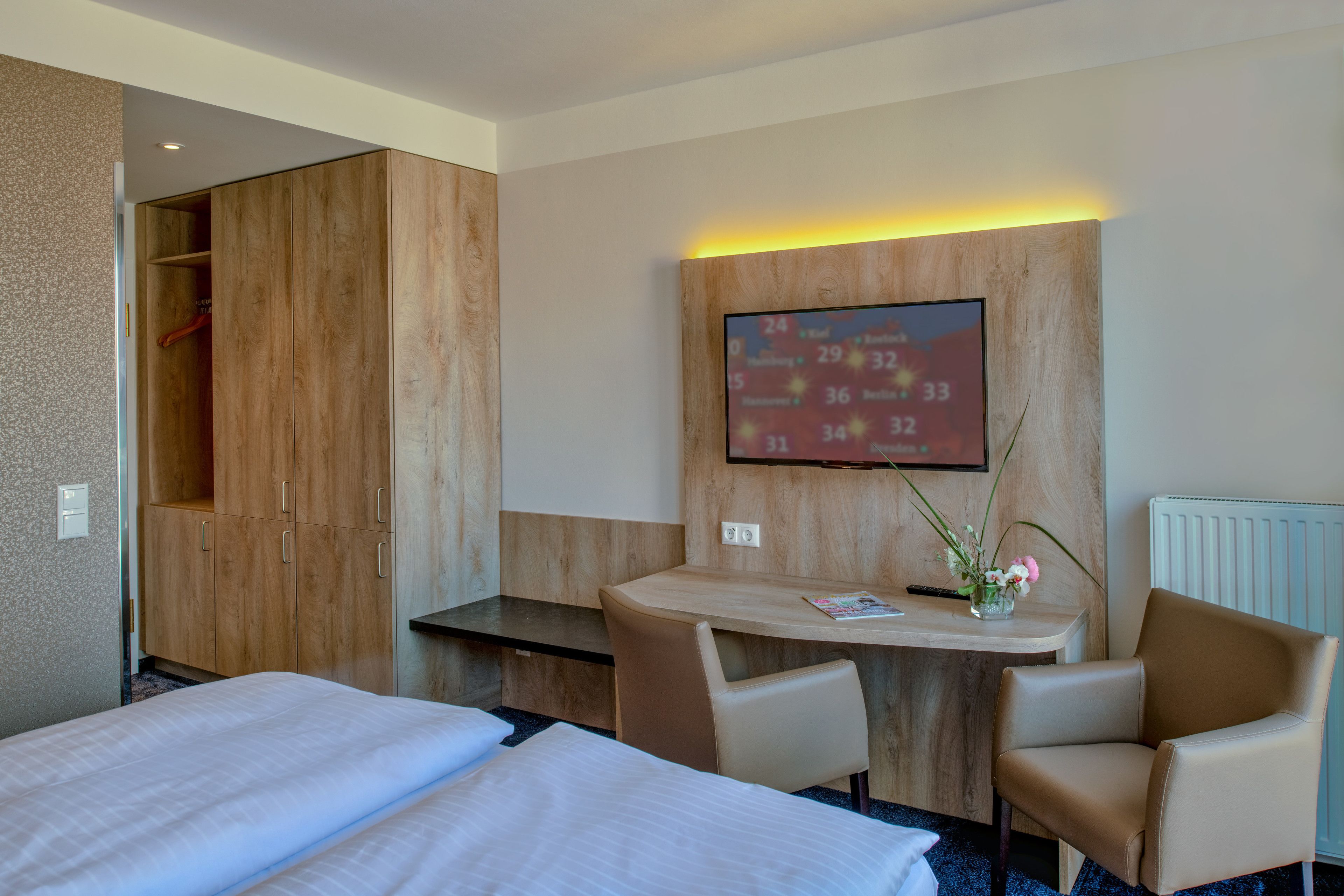 Une chambre d’hôtel avec deux lits, un bureau, une chaise, un téléviseur fixé au mur et une armoire.