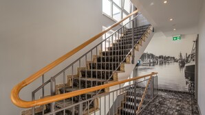 A staircase with wooden handrails and metal railings, leading to a room with a large mural of a harbor scene. - Pension StromInn (Rostock)
