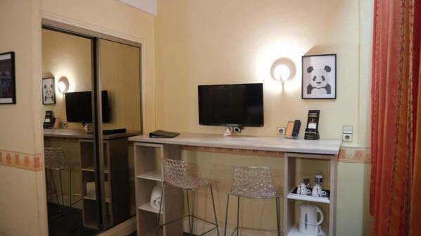 Una habitación de hotel con un escritorio, dos taburetes altos, un televisor, un cuadro de un panda y un espejo.