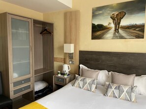 A hotel room with a bed, a wardrobe, a nightstand, a lamp, and a painting of an elephant on the wall. - Contact Hôtel le Provence (Agen)