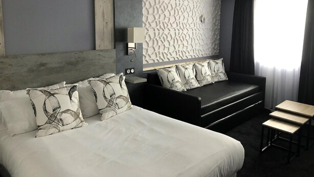 A modern hotel room with a large bed, a sofa, a small table, and a decorative wall panel. - Contact Hôtel le Provence (Agen)