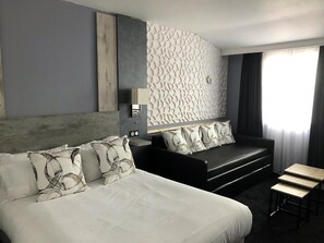 A modern hotel room with a large bed, a sofa, a small table, and a decorative wall panel. - Contact Hôtel le Provence (Agen)