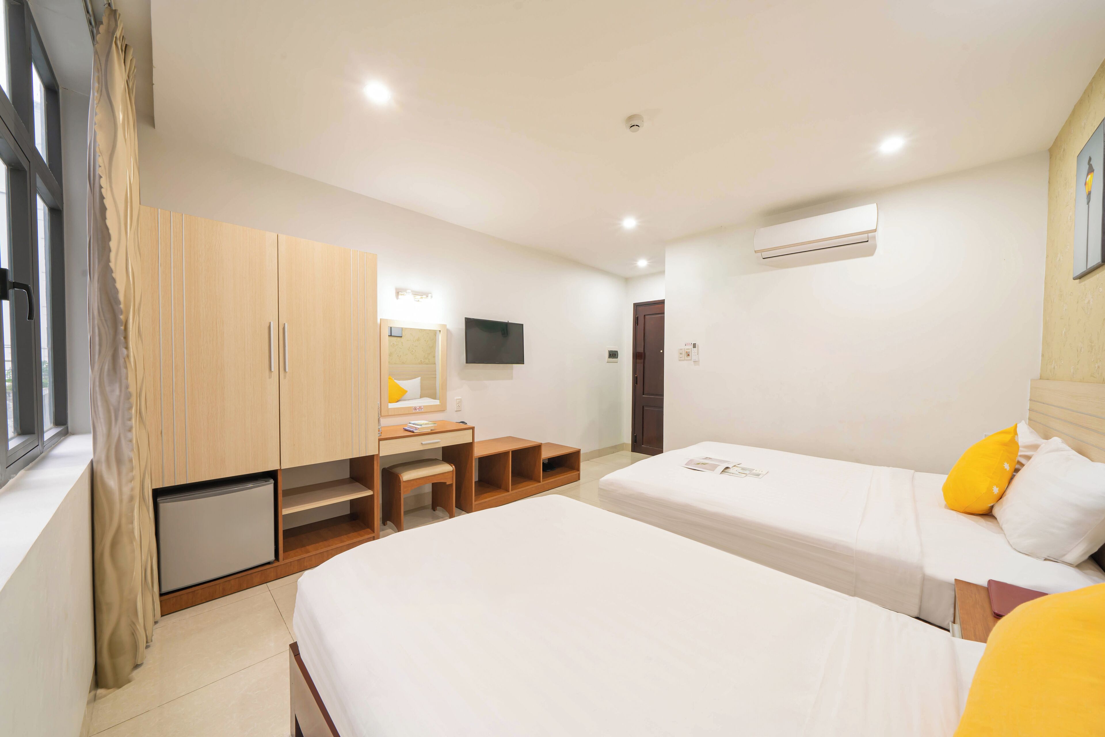 A hotel room with two beds, a desk, a chair, and a TV.