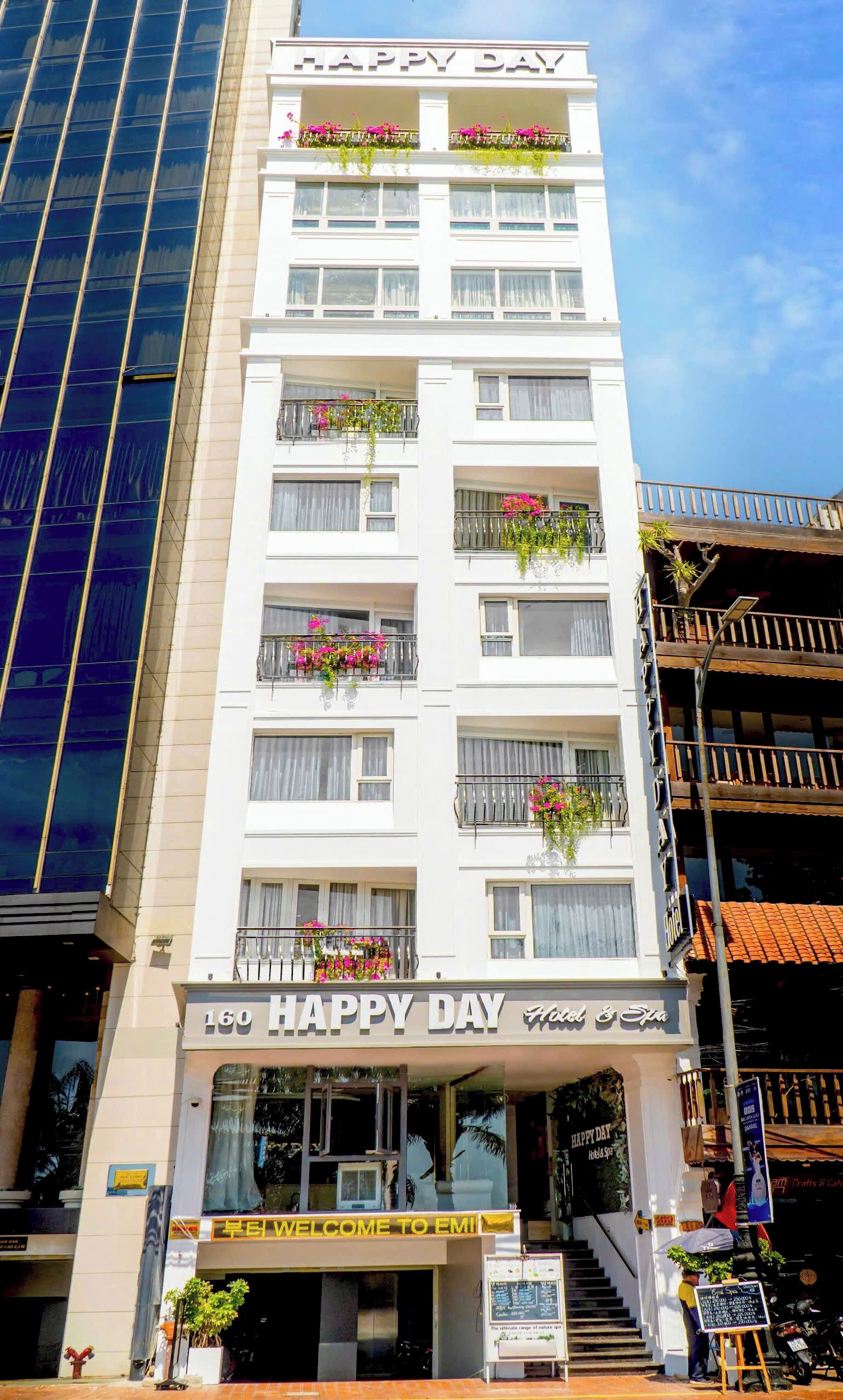 A multi-story hotel with balconies adorned with flowers, a sign reading "HAPPY DAY Hotel & Spa", and a welcoming entrance.
