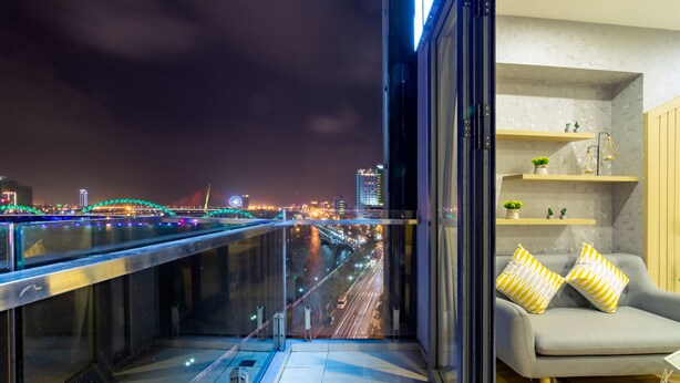 A modern living room with a balcony overlooking a cityscape at night. - Happy Day Riverside Hotel & Spa Danang (Da Nang)