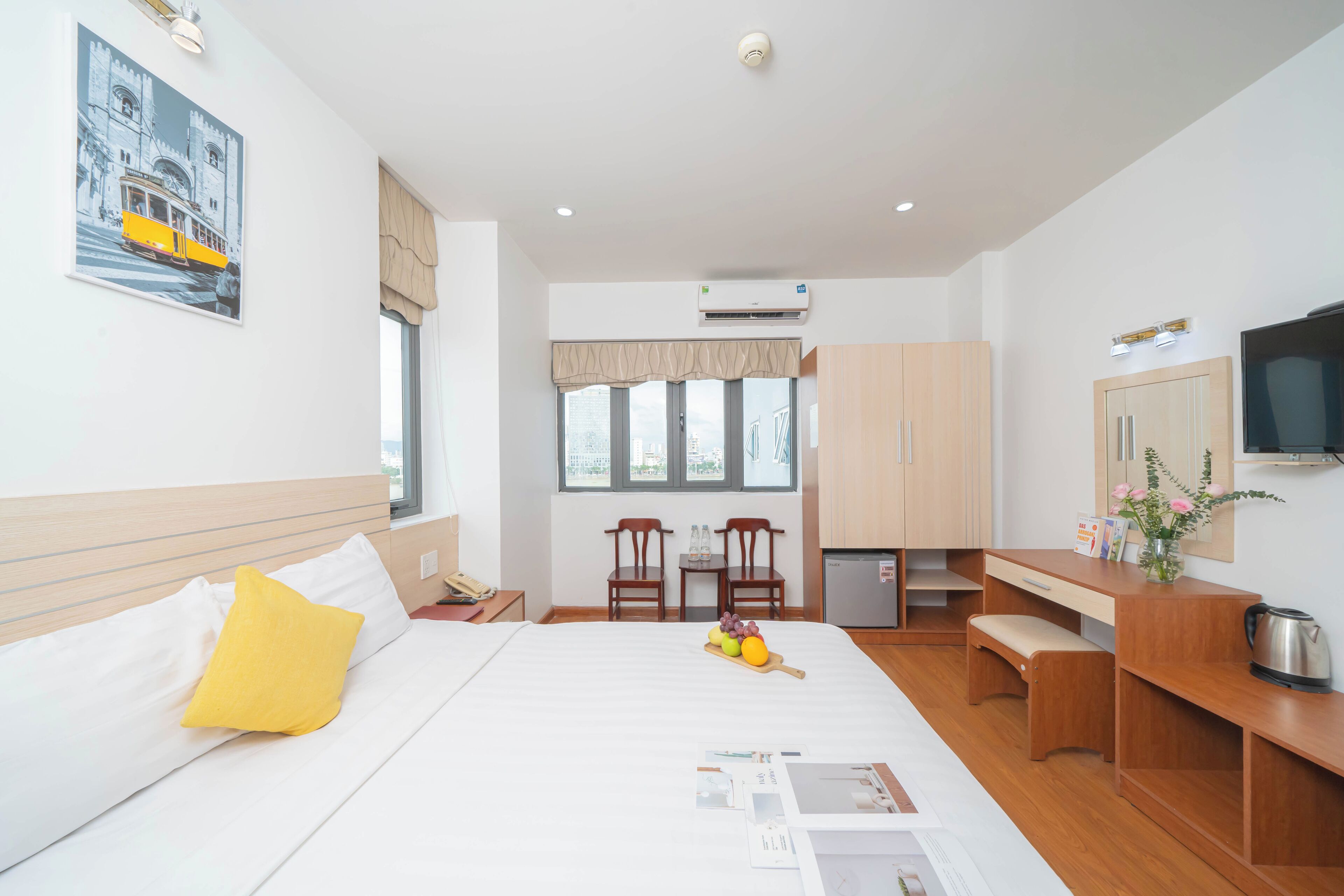 A hotel room with a bed, a desk, a chair, a kitchenette, and a TV.