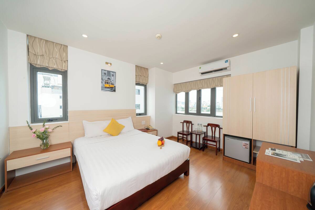 A hotel room with a large bed, bedside tables, a desk, and a small refrigerator.