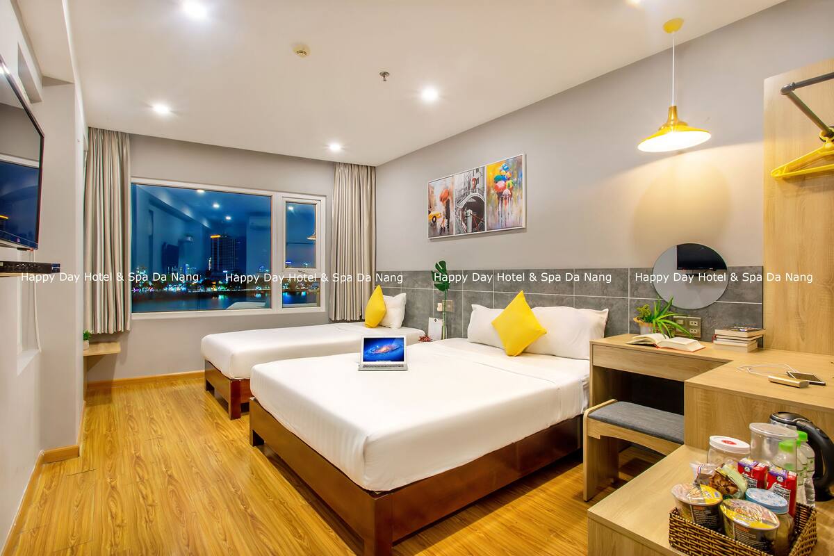 A hotel room with two beds, a desk, a TV, and a window with a city view.