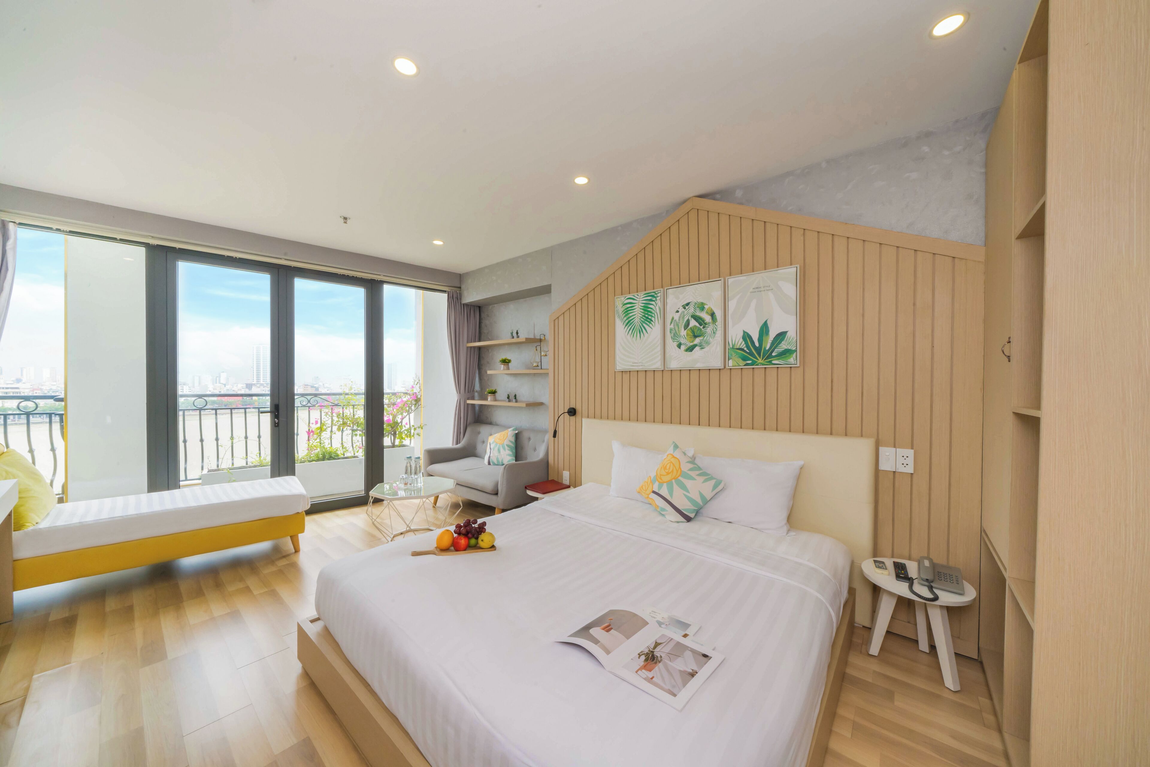 Quarto de hotel moderno com uma cama grande, um espaço de estar pequeno, uma varanda com vista para a cidade e uma parede de destaque em madeira.