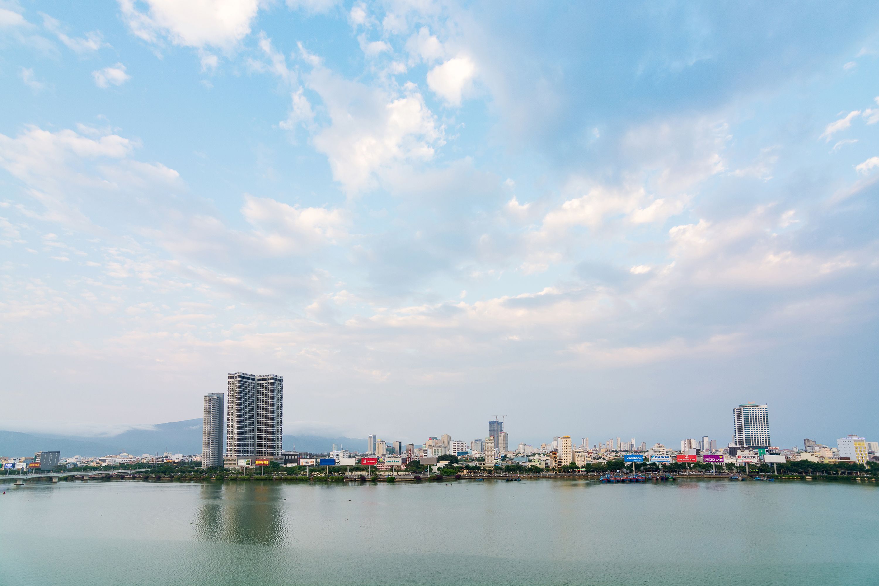 A city skyline with high-rise buildings and a calm body of water in the foreground.